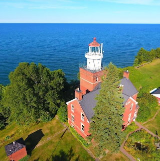 Aerial view of a red lighthouse building beside the blue ocean on a grassy headland