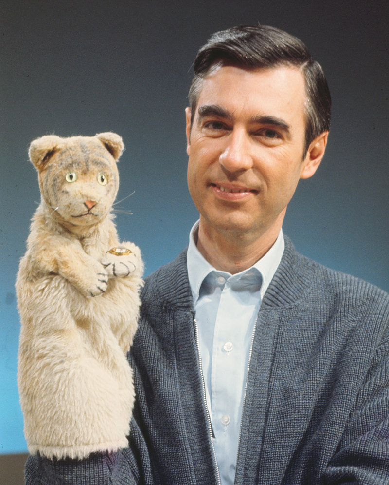 Fred Rogers smiling in blue cardigan holding Henrietta Pussycat puppet