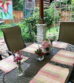 Patio table with striped placemats, flower vases, and chairs in a garden setting