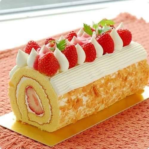 Strawberry swiss roll cake with cream filling, topped with strawberries, white chocolate drizzle, and mint garnish