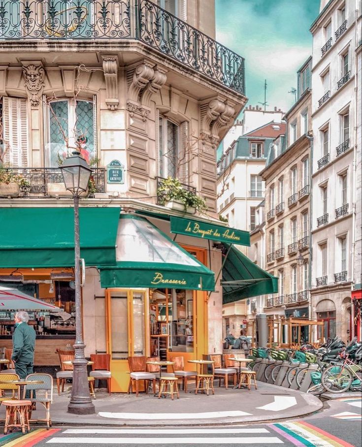 Parisian cafe with green awning on corner with outdoor seating and rainbow crosswalk