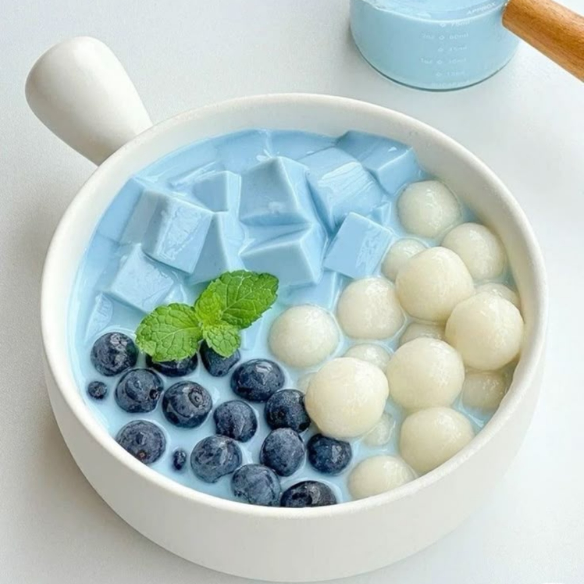 Bowl of blue jelly cubes with white sago pearls, blueberries and mint in coconut milk