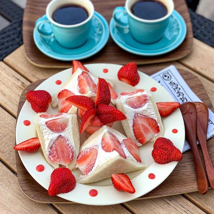 Two cups of black coffee with strawberry fruit sandwiches on a plate and tray