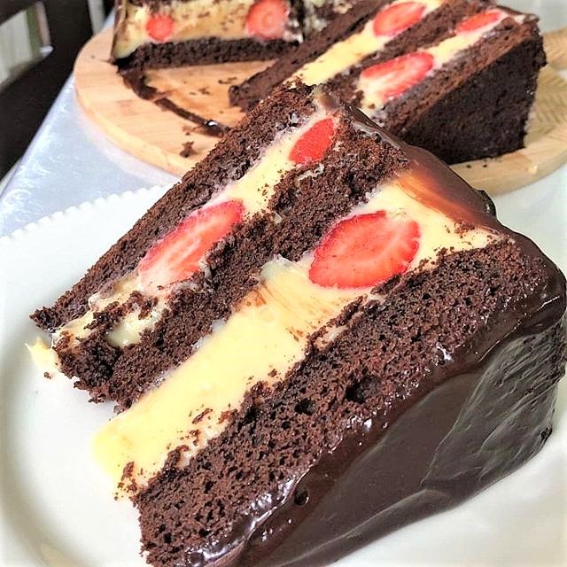 Close-up of a chocolate layer cake slice with cream filling and strawberry pieces on a white plate