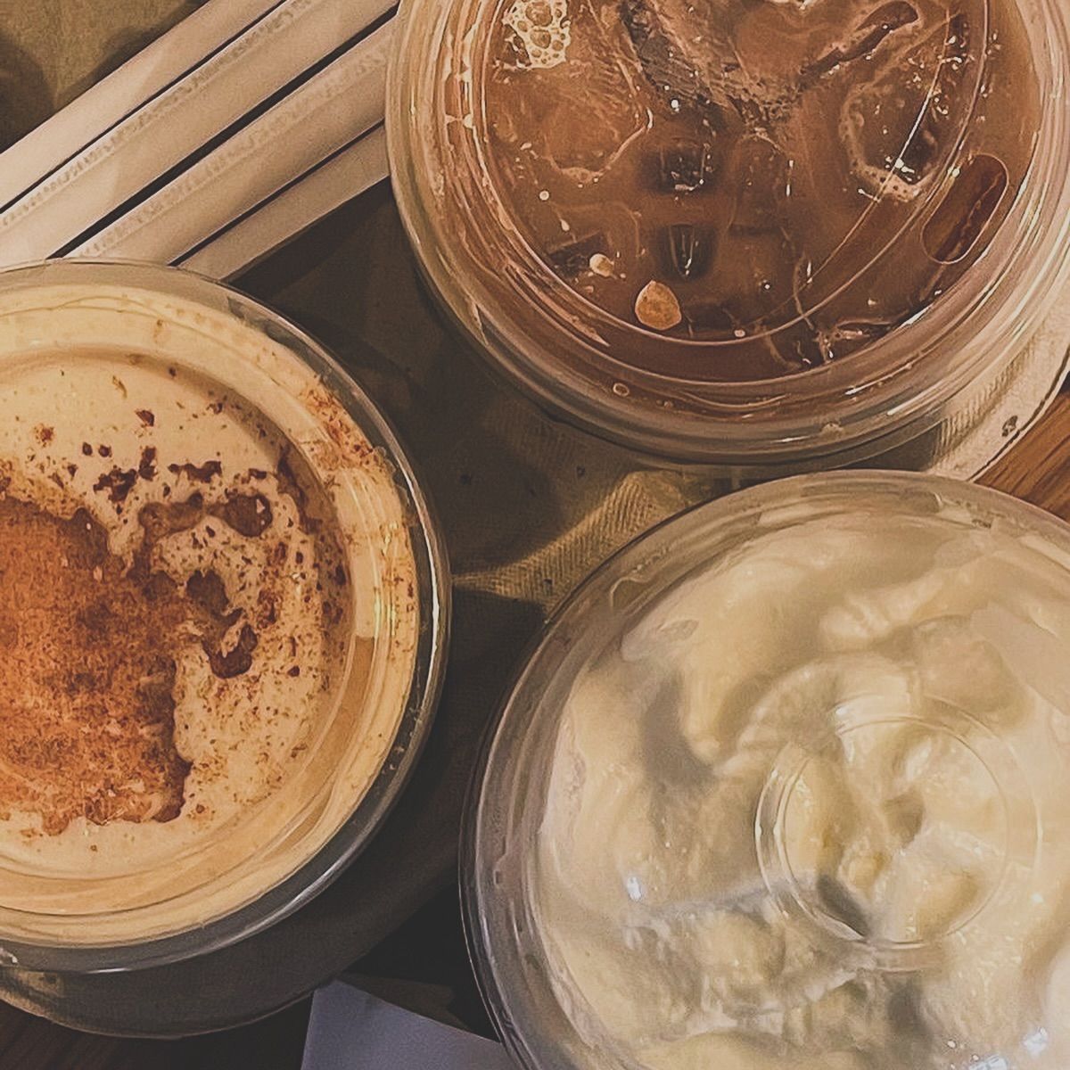 Three iced coffee drinks with whipped cream viewed from above on wooden table