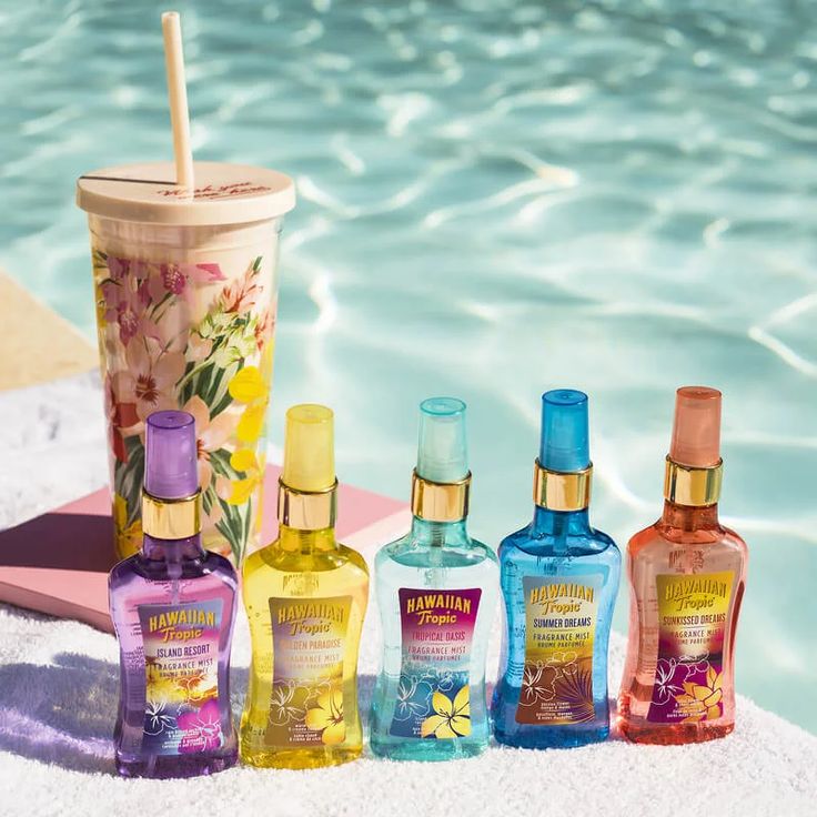 Hawaiian Tropic fragrance bottles in various colors lined up beside a tropical drink by a pool