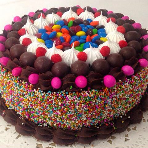 Chocolate cake with rainbow sprinkles, colorful candy, chocolate balls, and whipped cream topping
