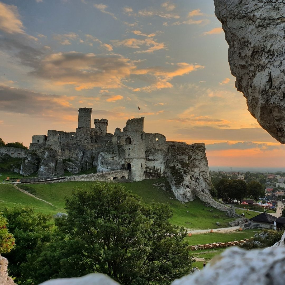 Ogrodzieniec Castle ruins on a rocky hill at sunset with green slopes and limestone cliffs