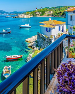 Greek island coastal scene with white houses, blue sea, boats, and purple flowers on balcony railing
