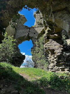 Old stone ruins with arched openings, blue sky above, and grass and shrubs in the foreground.