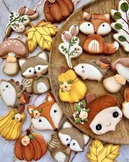 Decorated autumn sugar cookies shaped like foxes, raccoons, hedgehogs, leaves, pumpkins, and mushrooms on a wooden tray
