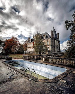 Abandoned mansion with empty pool in foreground, dramatic sky overhead