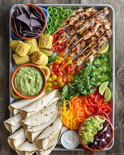Overhead view of a grilled chicken salad platter with colorful vegetables, chips, and dips on a wooden serving tray