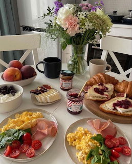 Breakfast table with eggs, toast and jam, fruit, coffee, yogurt, and flowers in a vase