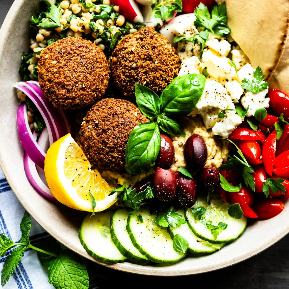 Mediterranean falafel bowl with fresh vegetables, cucumber, tomatoes, olives, feta, lemon, and pita bread