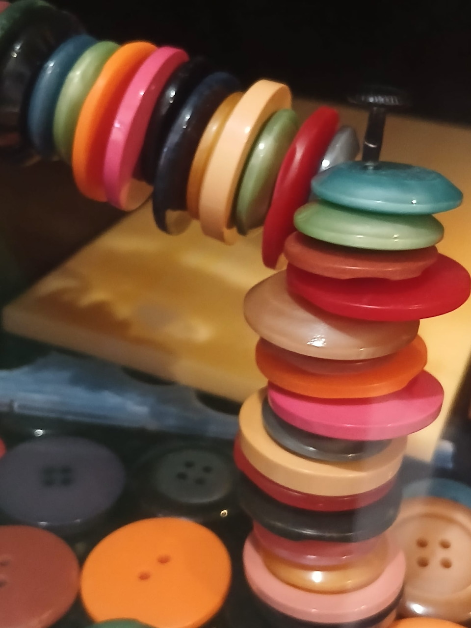 Stack of colorful buttons on a wire with scattered buttons on a wooden surface