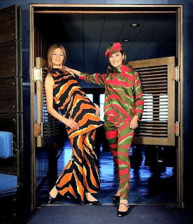 Two women posing in a doorway wearing bold patterned outfits, one in orange-black and the other in red-green
