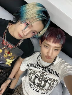 Two young men with blue-blonde and purple-red dyed hair taking a selfie wearing graphic tees and chains