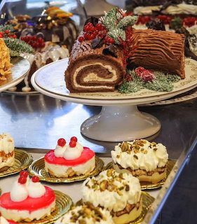 Chocolate yule log cake with berries and pine on a cake stand, surrounded by mini tarts with red and white toppings