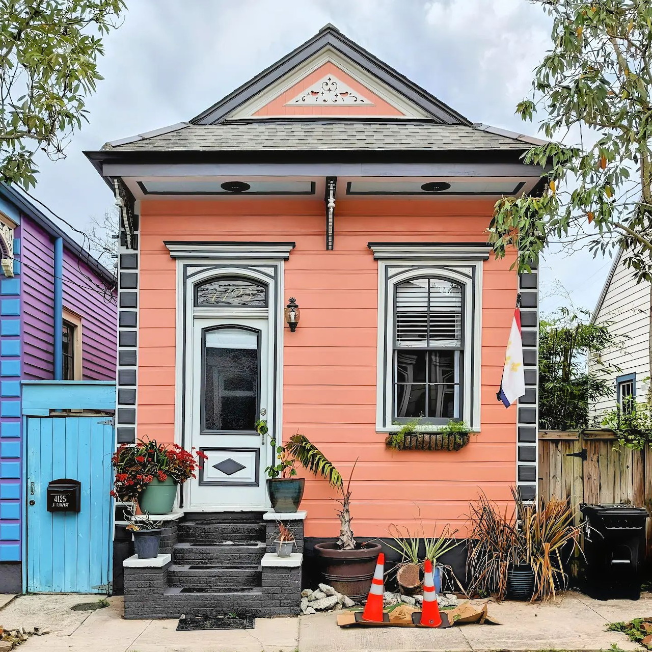 Peach colored house with gray roof, white shuttered windows, black steps, and blue gate surrounded by greenery