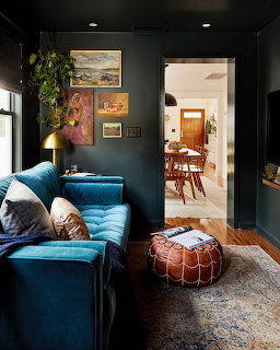 Moody living room with a turquoise sofa, wall art, leather pouf, and doorway to a dining room