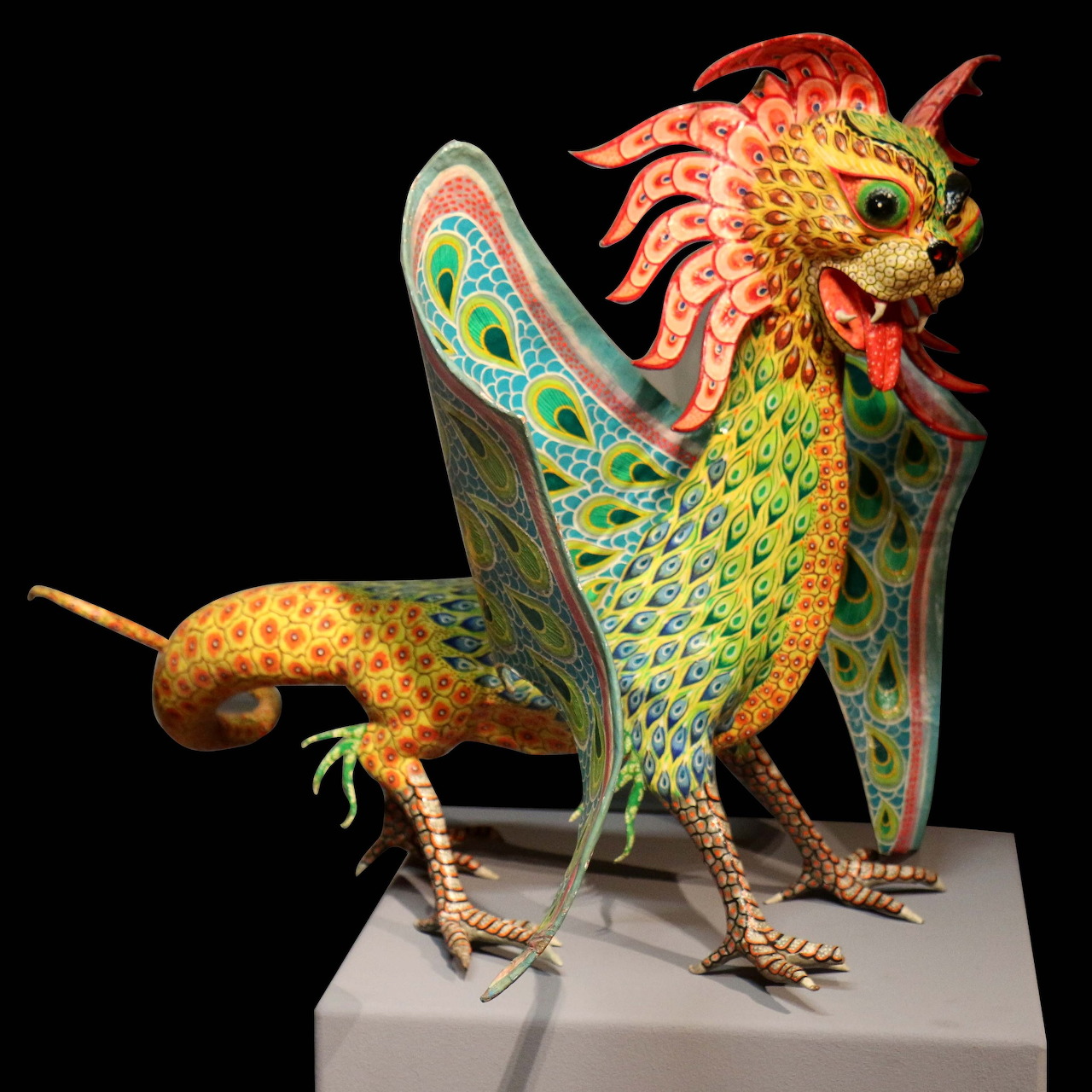 Vibrant Mexican alebrije folk art sculpture of a dragon-like creature with yellow scales, green wings, and red accents