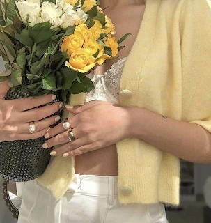 Woman in yellow cardigan holding a bouquet of yellow and white roses with rings on her hands