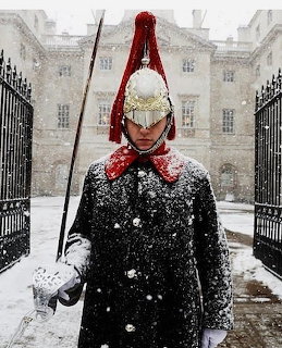 British Royal Horse Guard in ceremonial uniform with silver helmet and sword standing in snowfall