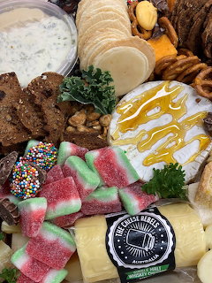 Overhead view of a charcuterie board with cheese, honey, crackers, pretzels, candies, and dip