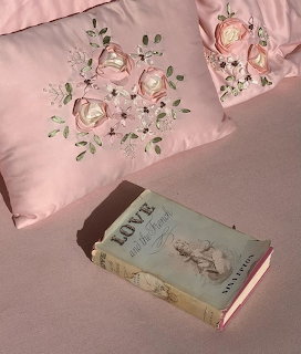 Blue vintage book on a pink bedspread with two pink floral pillows