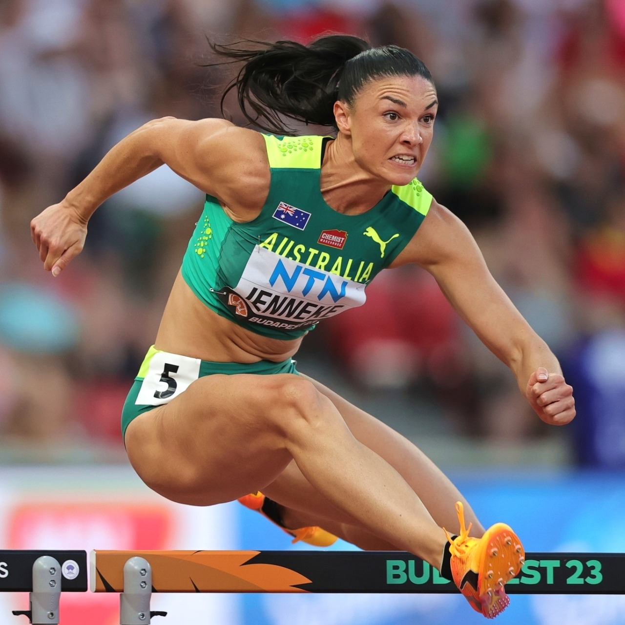 Female Australian hurdler jumping over a hurdle on a track