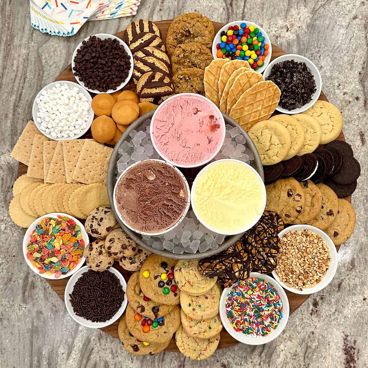 Ice cream sandwich board with cookies, wafers, sprinkles and various ice cream flavors in bowls
