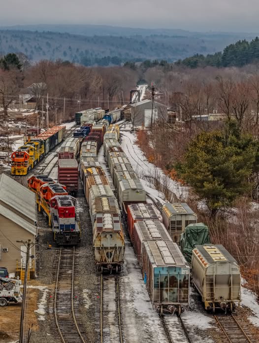 Overhead view of a snowy train yard with colorful freight locomotives and cars on multiple parallel tracks