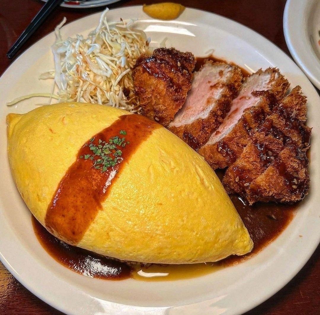 Plate of omurice with brown sauce, sliced fried cutlet, and shredded cabbage