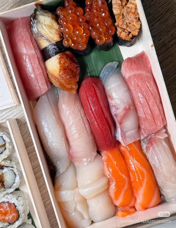 Wooden box of assorted nigiri sushi with salmon, tuna, scallop and roe toppings, plus maki rolls on the side.