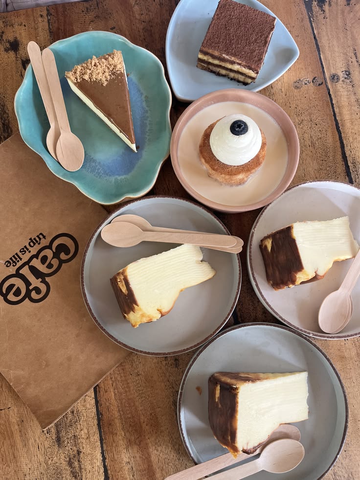 Top-down view of five dessert plates with cake slices and a cream puff on a wooden table