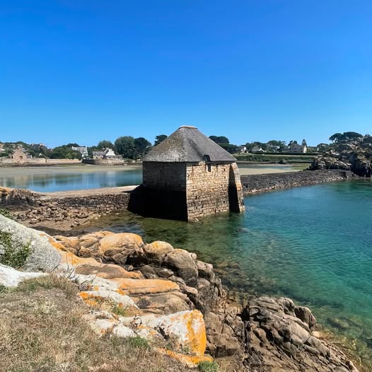 Stone hut on a rocky shore beside turquoise water under a clear blue sky