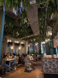Cozy cafe interior decorated with hanging purple wisteria, lanterns, and greenery above dining tables