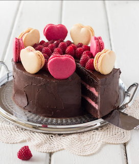 Round chocolate cake decorated with raspberries and pink macarons on a glass stand