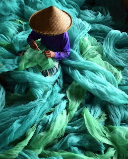 Person in a conical hat surrounded by turquoise fishing nets seen from above