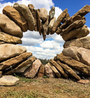 Balanced stacked stones forming an arch with blue sky and clouds visible through the opening