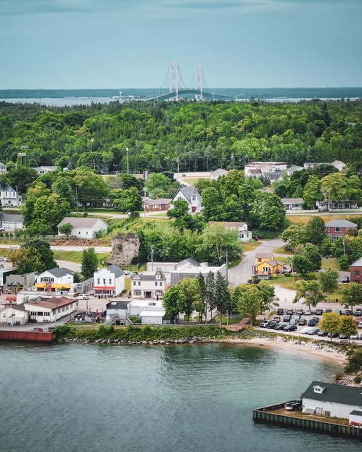 Aerial view of St. Ignace waterfront with marina, residential area, trees, and distant bridge