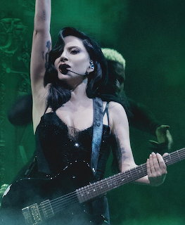 Woman in black performing on stage with an electric guitar and headset microphone