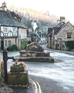 Historic stone cottages and a curved village road with a market cross in Castle Combe