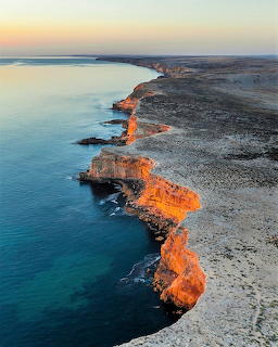 Aerial view of rocky coastline with turquoise water and orange sunset light on cliffs at Eyre Peninsula Australia