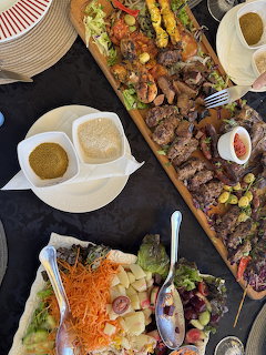 Overhead view of a Moroccan BBQ platter with grilled meats, skewers, sauces, salad, and bread