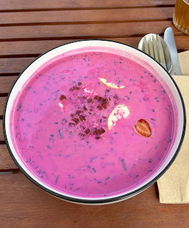 Bowl of bright pink chlodnik cold beetroot soup with egg garnish on a wooden table