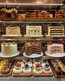 Glass bakery display case with multiple shelves of cakes, pastries, macarons, and desserts