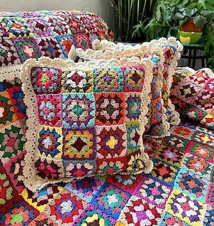 Colorful crocheted granny square pillow and blankets on a couch with plants