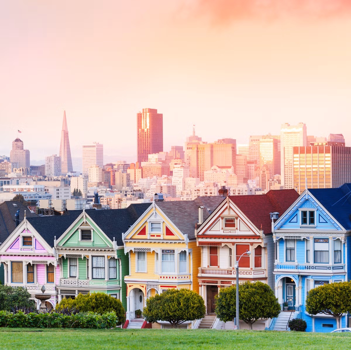 Colorful Victorian Painted Ladies houses in a row with San Francisco skyline behind at sunset